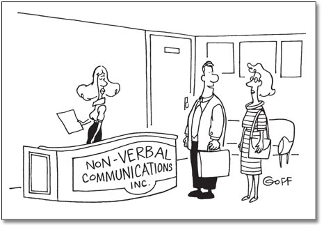 This is a cartoon image. It shows an office reception area. A receptionist stands behind a desk. A sign on the front of the desk reads ‘Non-Verbal Communications Incorporated’. A man and woman stand in front of the desk. The man is speaking to the woman. The caption of the cartoon reads. ‘See? That means, “What do you clowns want?”’